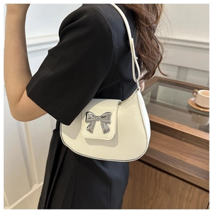 Detail of a beige crescent bag with a silver bow accent shown on model in a cafe