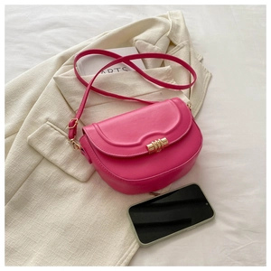 Detail view of magenta saddle bag with wavy flap and gold buckle next to a smartphone
