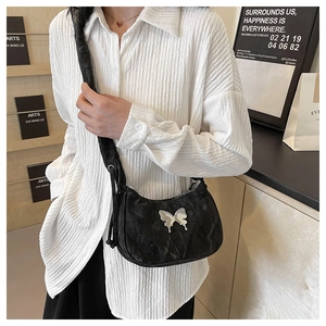 Detail of a black pleated shoulder bag featuring a metallic silver butterfly buckle charm