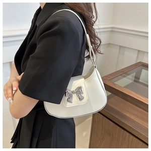 Detailed side view of white crescent bag featuring a metallic silver bow and slim strap