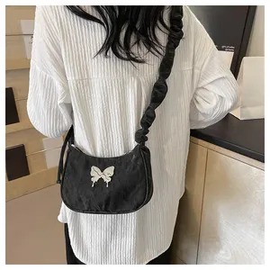 Close-up of black ruched shoulder bag featuring a silver metal butterfly and pleated strap