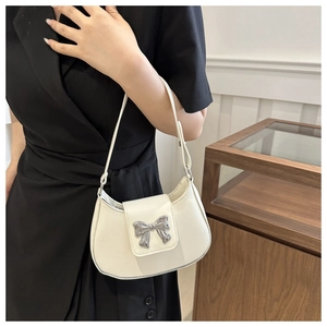 Close-up of cream white shoulder bag featuring a polished silver bow-knot metal buckle