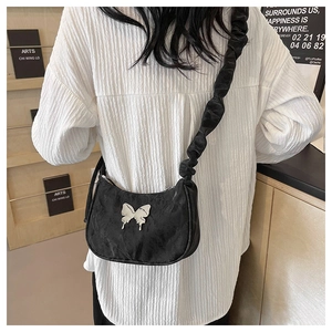 Close-up of black crescent bag with silver butterfly emblem and pleated strap detail