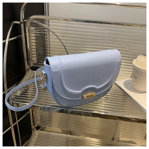 Close-up of light blue saddle bag with wavy flap and gold cylindrical twist lock