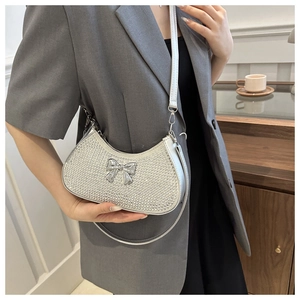 Detail of silver rhinestone half-moon shoulder bag with metallic bow on grey suit