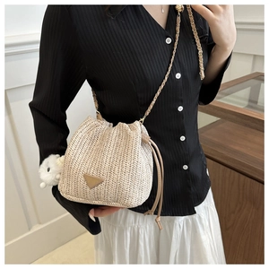 Detail of a beige straw bucket bag with drawstring and chain strap on a model