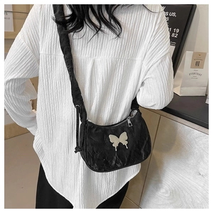 Detail of black pleated crossbody bag featuring a silver butterfly metal ornament
