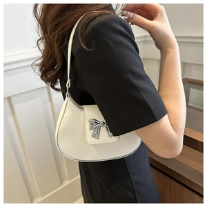 Detail of a white half-moon shoulder bag with a silver metal bow buckle on a faux leather finish