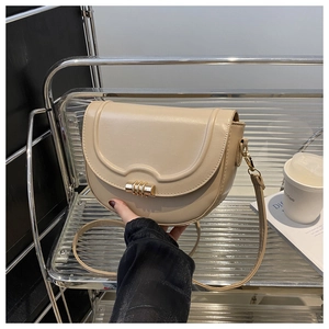 Close-up of elegant beige saddle bag featuring unique gold spiral metal buckle detail