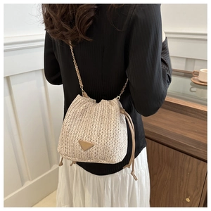 Detail of beige straw bucket bag with V-weave texture and gold chain strap on model
