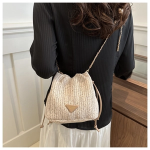 Detail of hand-woven straw bucket bag with triangle metal logo and chain strap