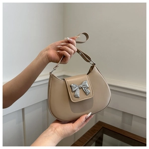 Detailed shot of a beige half-moon bag featuring a 3D silver metal bow and leather strap