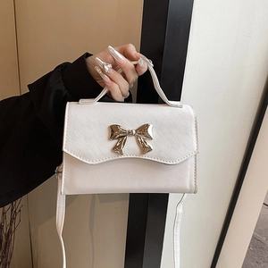 Elegant white crossbody square bag with gold bow clasp, shown being held indoors