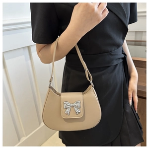 Detail of beige saddle bag featuring a silver bow buckle and smooth leather texture