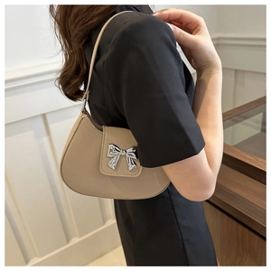 Detail of a chic beige underarm bag featuring a large silver metallic bow decoration