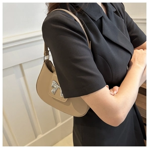 Close-up of beige hobo bag featuring a metallic silver bow clasp and matte leather texture