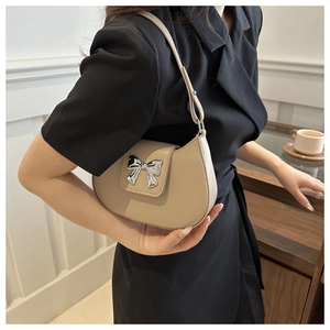 Detail of light khaki shoulder bag with silver bow accent on model in elegant scene