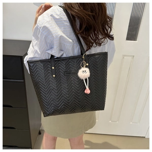Detail of black V-quilted tote bag featuring metallic rivets and a white pompom charm