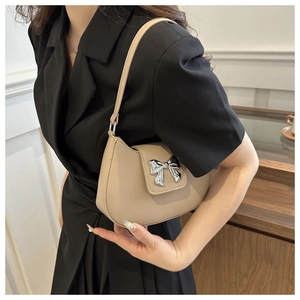 Detail of minimalist beige shoulder bag with silver bow buckle worn on a model's arm