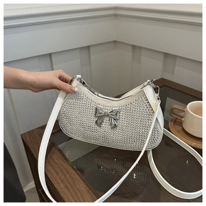 Detailed view of a white crescent shoulder bag with rhinestones and a metal bow ornament
