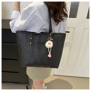 Detail of black quilted tote bag with V-pattern and white pom-pom charm on shoulder