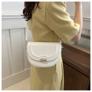 Close-up of white saddle bag with golden twist lock on shoulder of model in yellow dress