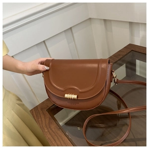 Detail of a brown leather saddle bag featuring a gold cylindrical twist lock and fine texture