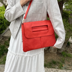 Sac bandoulière rouge en cuir grainé avec poignée, porté par un mannequin en extérieur