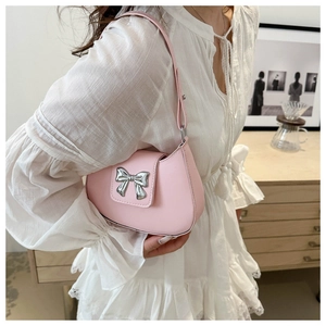 Detail of pink saddle bag featuring a decorative silver metallic bow on the smooth leather flap