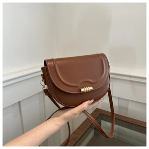 Detail of a brown saddle bag featuring a gold metal clasp and adjustable shoulder strap