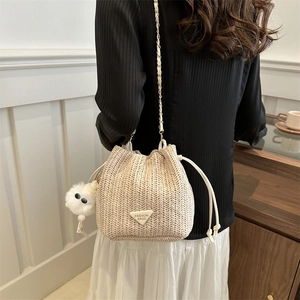 Straw drawstring bucket bag with chain strap and cute plush charm on a female model