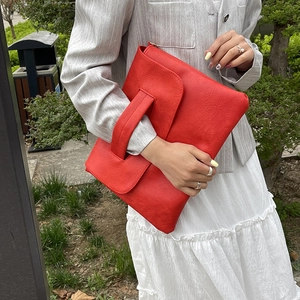 Pochette élégante en cuir rouge avec poignée portée sur un blazer gris et une jupe blanche