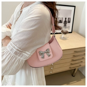 Detail of pink leather saddle bag featuring a shiny silver metal bow and shoulder strap