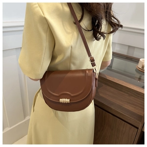 Close-up of brown leather saddle bag with gold cylinder lock on a yellow dress