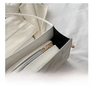 Close-up of white quilted bag showing the smooth gold metal zipper and black lining
