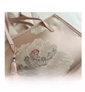 Close-up of pink silk shoulder bag with elegant floral embroidery and tassel detail