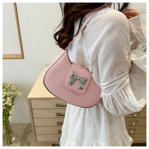 Detailed view of pink shoulder bag with silver bow ornament worn by a model