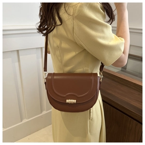 Brown leather saddle bag with gold cylinder buckle worn as a crossbody shoulder bag