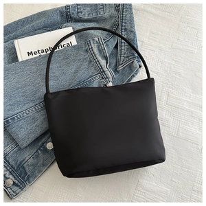 Detail of a black minimalist nylon bucket bag on a white textured fabric background