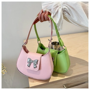 Close-up of pink and green handbags with large silver metal bow buckles on wooden surface