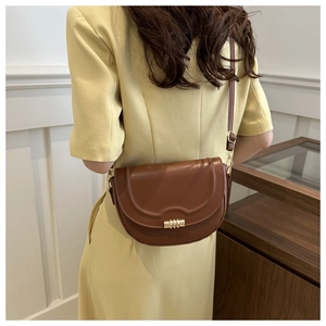 Nahaufnahme der karamellfarbenen Satteltasche mit goldenen Details am gelben Kleid