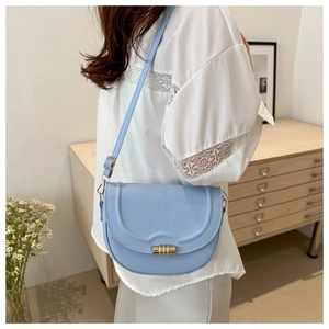 Close-up of light blue saddle bag with gold metal cylinder lock and fine stitching detail