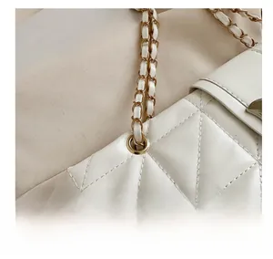 Detailed macro shot of premium quilted leather texture and gold chain strap on white tote bag