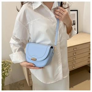 Elegant light blue leather saddle bag with gold buckle on a stylish wooden cabinet