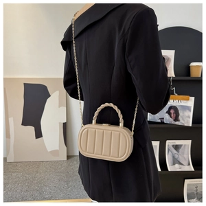 Dettaglio di una borsa a scatola kaki con nervature verticali e tracolla a catena dorata