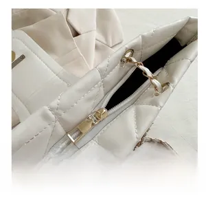 Detail of a smooth gold metal zipper on a white quilted shoulder bag with black lining