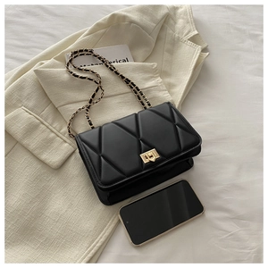 Detail of black quilted crossbody bag with gold chain strap and smartphone for size scale