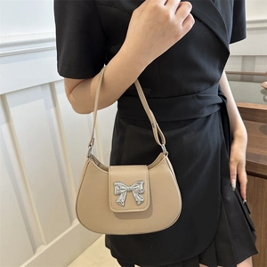 Beige crescent shoulder bag with silver bow accent on a model in a black dress