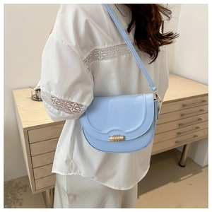 Detail of light blue saddle bag with wavy flap and golden cylindrical metal twist lock