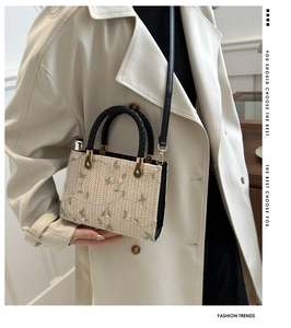 Close-up of woven bag showing delicate floral embroidery and black braided handle